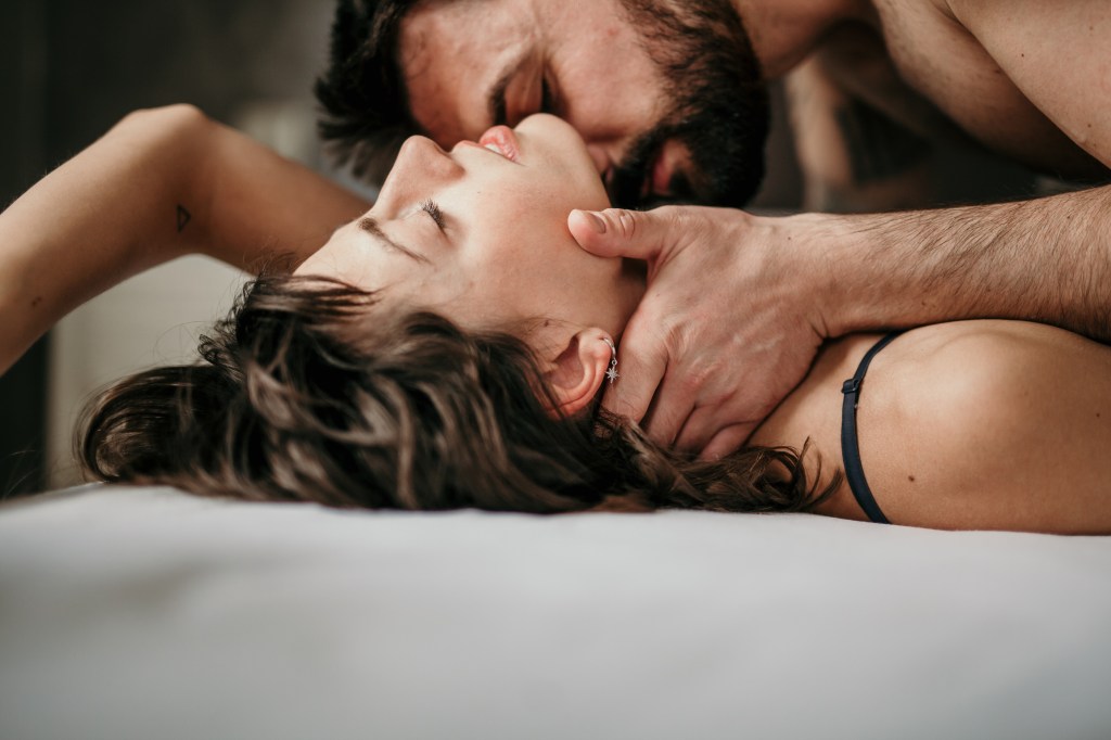 Side view of bearded man gently kissing neck of brunette woman in bed, eyes closed in pleasure